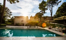 Scenic view of a luxurious swimming pool surrounded by lush greenery and elegant sun loungers, with a charming villa in the background, capturing a beautiful sunset ambiance.