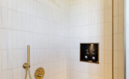 Modern shower design featuring a gold rain showerhead, sleek handheld faucet, and built-in niche for toiletries against a backdrop of white tiled walls. The spacious layout includes a built-in bench for added comfort.