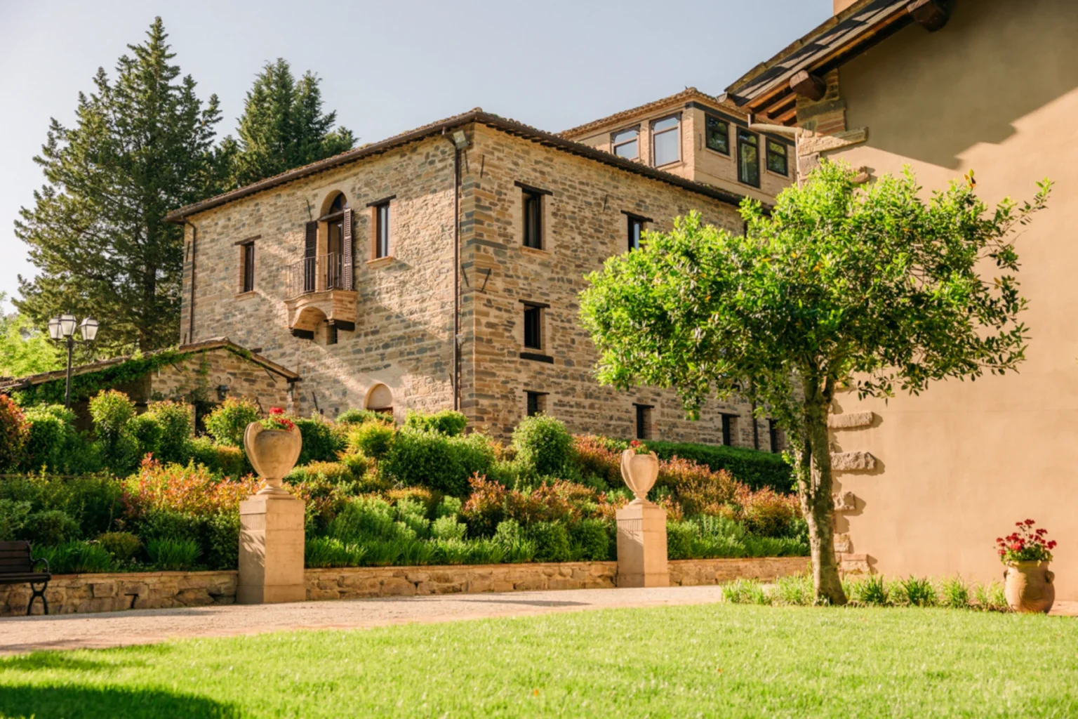 Historic stone building surrounded by lush greenery and landscaped gardens, featuring a balcony and decorative planters in a serene outdoor setting. Ideal for showcasing architectural beauty and natural surroundings. | Only on SopranoVillas