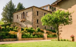 Historic stone building surrounded by lush greenery and landscaped gardens, featuring a balcony and decorative planters in a serene outdoor setting. Ideal for showcasing architectural beauty and natural surroundings.