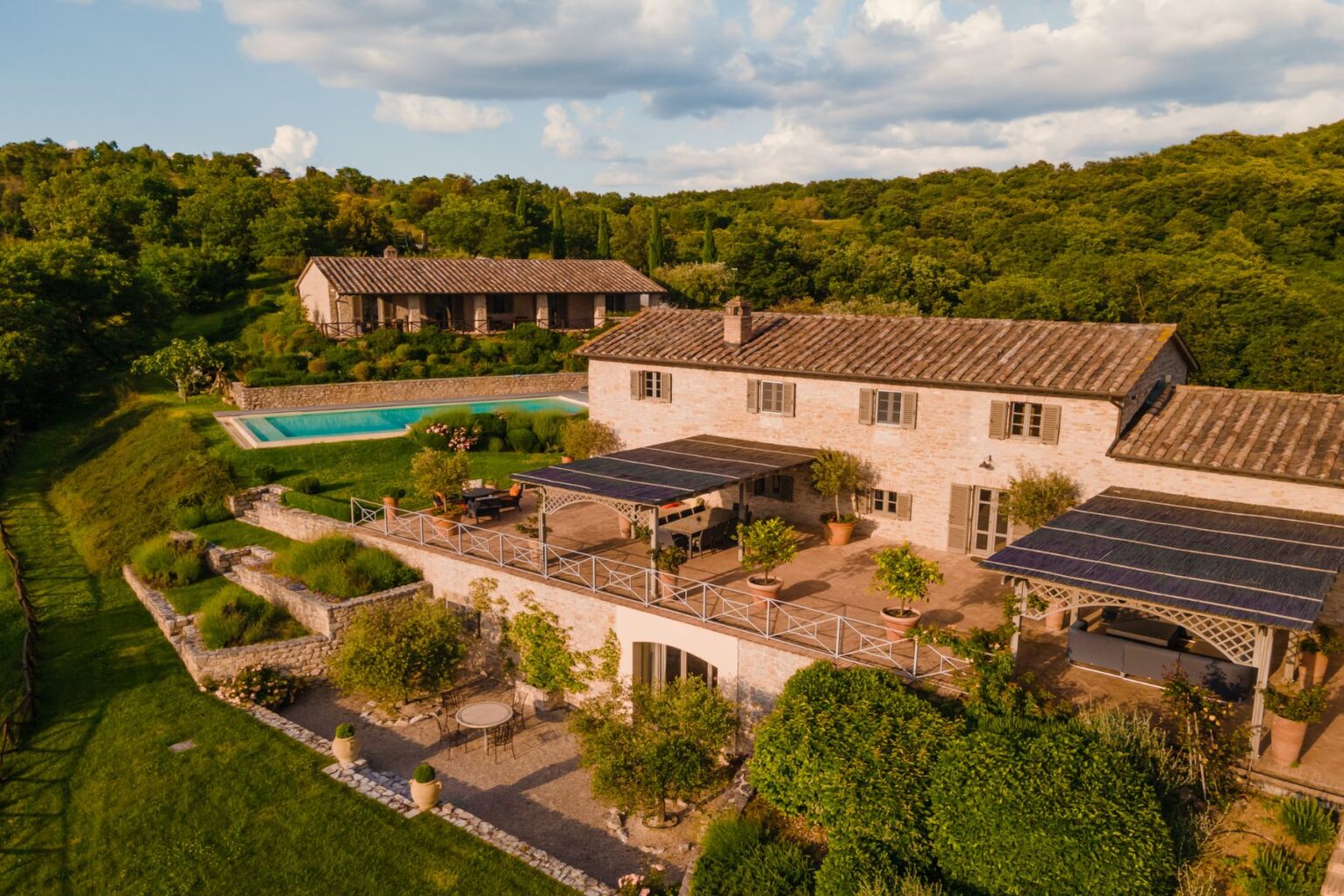 Aerial view of a charming stone villa surrounded by lush greenery, featuring a swimming pool, solar panels, and landscaped gardens, ideal for a serene getaway. | Only on SopranoVillas