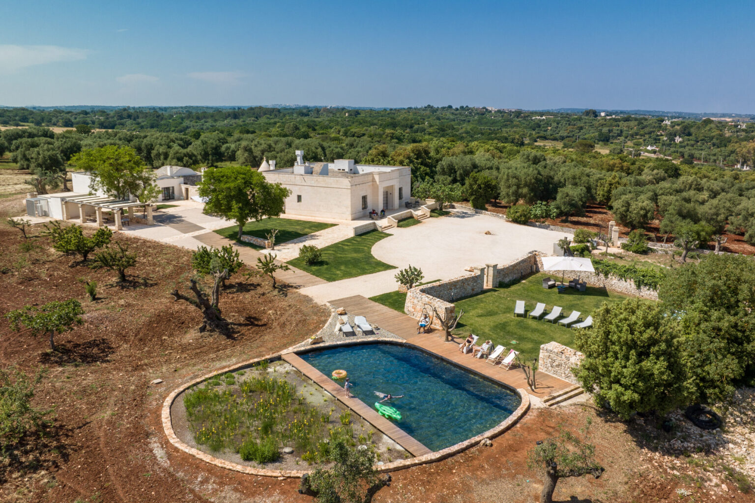 Aerial view of a luxurious villa surrounded by lush greenery, featuring a spacious outdoor area, a swimming pool, and comfortable lounge chairs. The property is set in a tranquil landscape, ideal for relaxation and outdoor activities. | Only on SopranoVillas