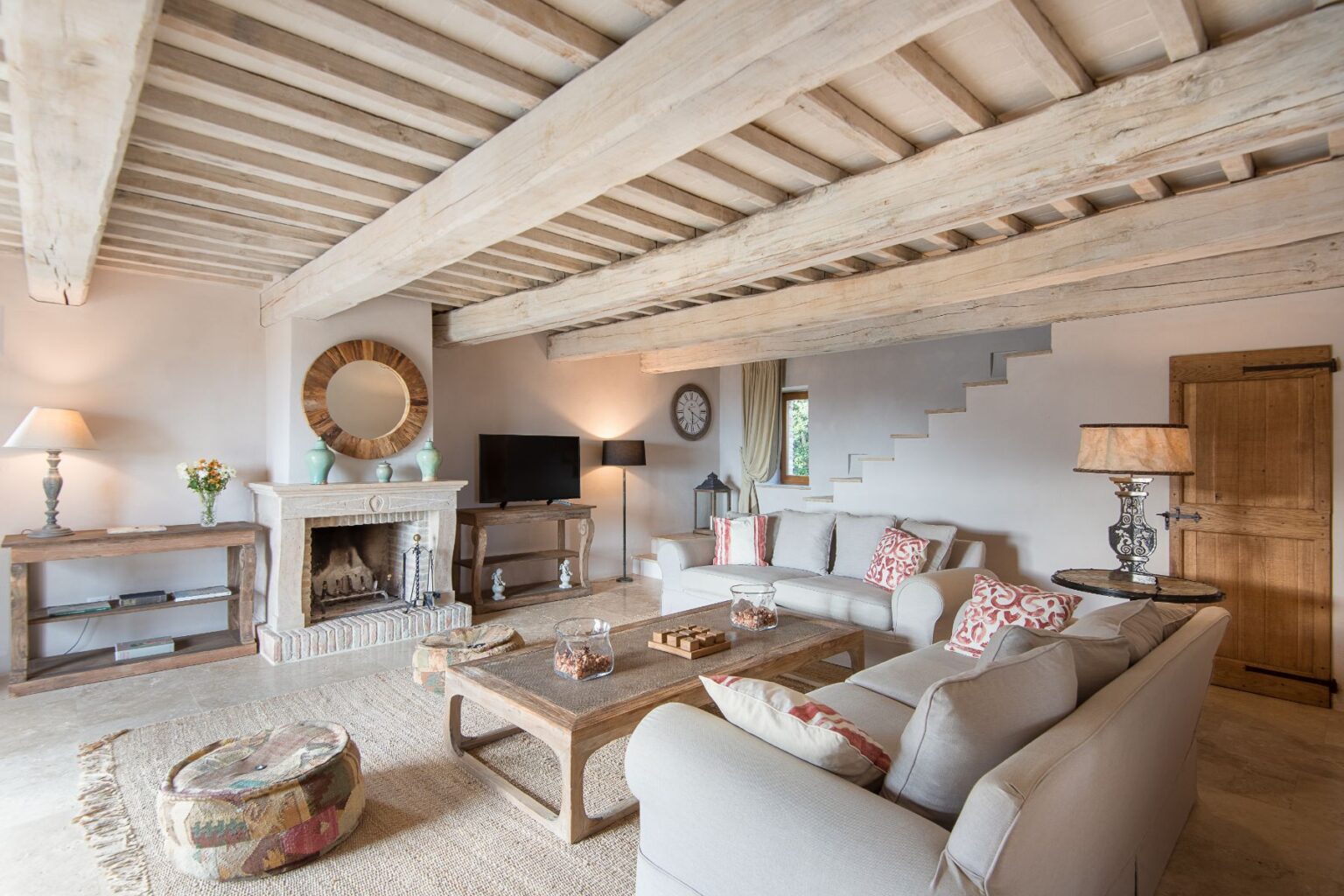 Cozy living room featuring exposed wooden beams, a stone fireplace, and stylish furnishings. The space includes a flat-screen TV, decorative accents, and a natural fiber rug, creating a warm and inviting atmosphere. | Only on SopranoVillas