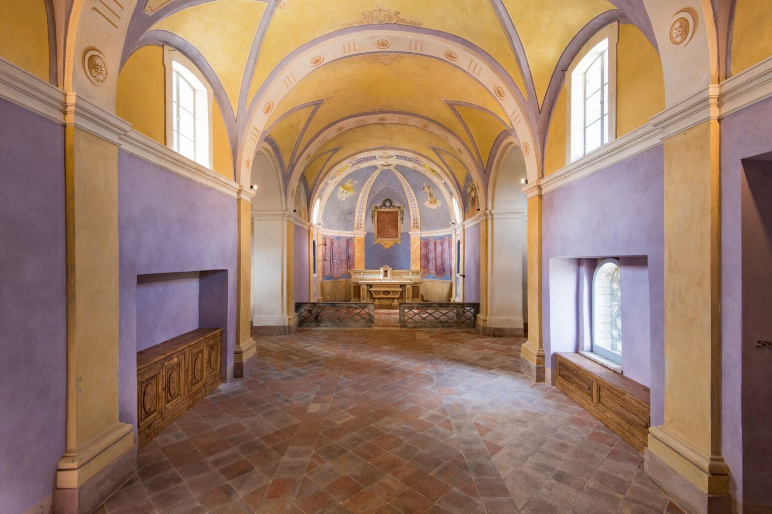 Interior view of a beautifully decorated chapel featuring arched ceilings, purple and yellow walls, and a wooden altar. The space is illuminated by natural light from windows, highlighting the intricate architectural details and serene atmosphere. | Only on SopranoVillas