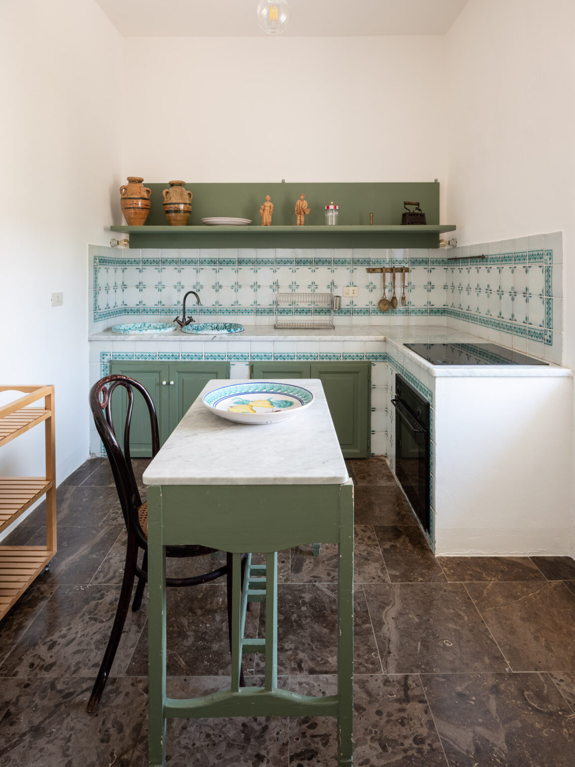 Bright and inviting kitchen featuring green cabinetry, patterned tile backsplash, and a marble tabletop. The space includes traditional pottery and wooden decor, along with modern appliances, creating a blend of rustic and contemporary design. | Only on SopranoVillas