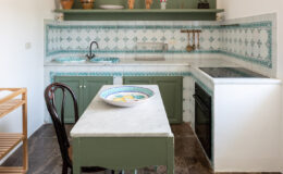 Bright and inviting kitchen featuring green cabinetry, patterned tile backsplash, and a marble tabletop. The space includes traditional pottery and wooden decor, along with modern appliances, creating a blend of rustic and contemporary design.