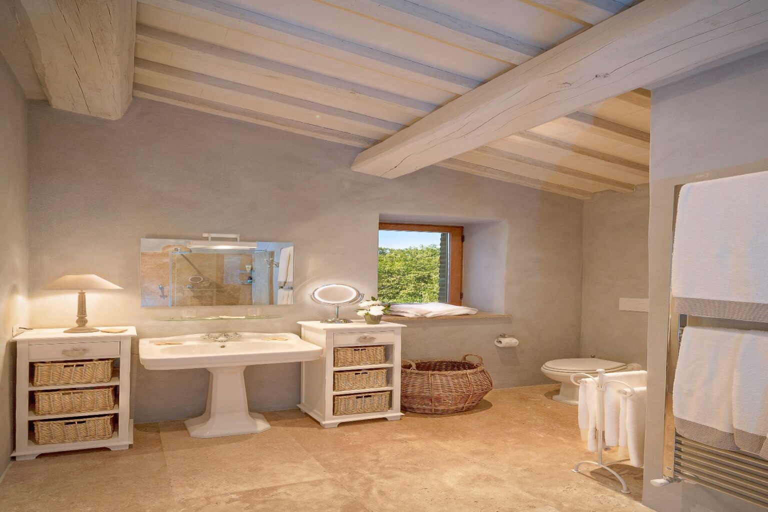 Modern bathroom interior featuring a white sink, a large mirror, and stylish storage solutions. Natural light floods in through a window, highlighting the elegant decor, including a lamp and decorative baskets. The space combines functionality with a serene, minimalist aesthetic. | Only on SopranoVillas