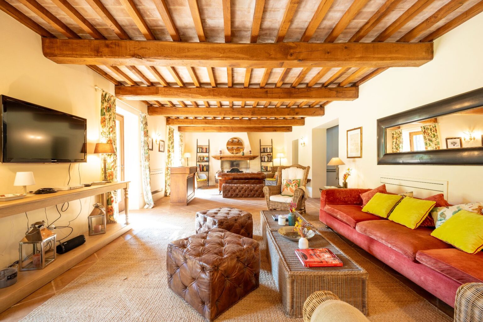 Spacious living room featuring wooden beams, a large flat-screen TV, and a cozy seating area with colorful cushions. The room includes a rustic coffee table, stylish lighting, and decorative curtains, creating a warm and inviting atmosphere. | Only on SopranoVillas