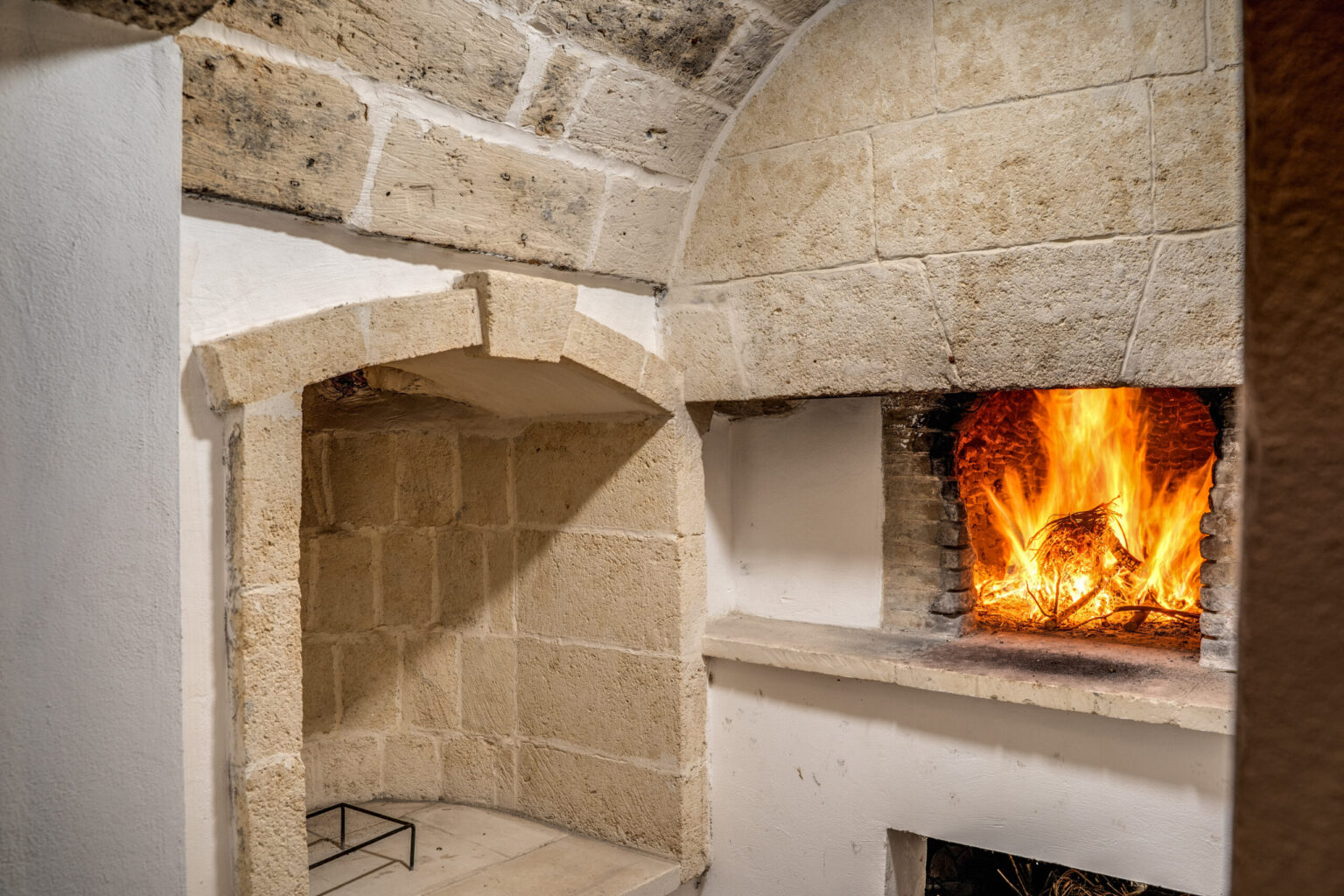 Cozy stone fireplace with a roaring fire in a rustic interior, featuring arched architecture and textured stone walls, ideal for creating a warm atmosphere. | Only on SopranoVillas