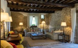 Cozy living room featuring rustic stone walls, wooden beams, and comfortable seating. Natural light filters through sheer curtains, illuminating stylish décor, including a coffee table and elegant lamps. Ideal for relaxation and inviting gatherings.