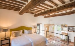 Spacious and stylish bedroom with a green upholstered headboard, two twin beds, wooden beams, and modern bathroom features, perfect for a cozy retreat.