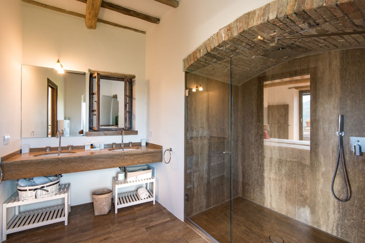 Modern bathroom design featuring a double sink with a wooden countertop, a large mirror, and a glass-enclosed shower. The space showcases natural light, rustic wooden beams, and stylish storage solutions. Ideal for luxury home inspiration. | Only on SopranoVillas