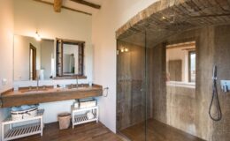 Modern bathroom design featuring a double sink with a wooden countertop, a large mirror, and a glass-enclosed shower. The space showcases natural light, rustic wooden beams, and stylish storage solutions. Ideal for luxury home inspiration.