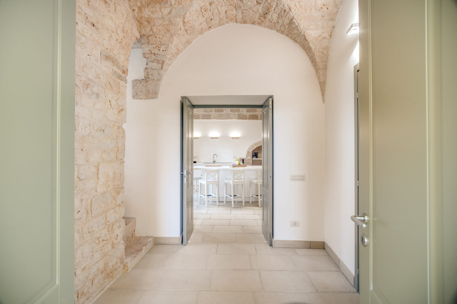 Interior view of a modern kitchen through an arched doorway, featuring stone walls and contemporary design elements, highlighting a spacious and inviting atmosphere. | Only on SopranoVillas