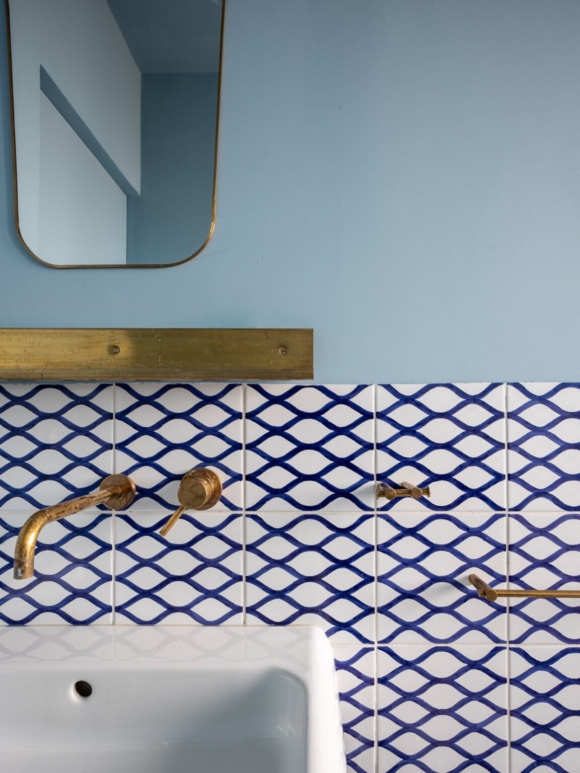 Modern bathroom design featuring a blue wall, decorative blue and white patterned tiles, brass fixtures, and a stylish mirror. Ideal for interior design inspiration. | Only on SopranoVillas