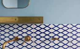 Modern bathroom design featuring a blue wall, decorative blue and white patterned tiles, brass fixtures, and a stylish mirror. Ideal for interior design inspiration.
