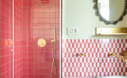 Modern bathroom design featuring a vibrant red tiled shower with a rain showerhead, complemented by a stylish gold faucet. The adjacent wall showcases a unique patterned tile design in shades of red, while a decorative mirror adds elegance to the space. Soft green walls enhance the overall aesthetic, creating a chic and contemporary atmosphere.