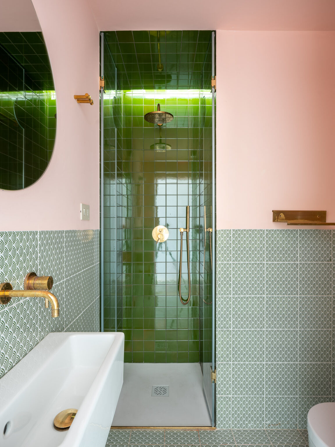 Modern bathroom featuring a green tiled shower with a gold showerhead, a white bathtub, and intricate green patterned tiles on the wall. Soft pink walls add warmth to the contemporary design. | Only on SopranoVillas