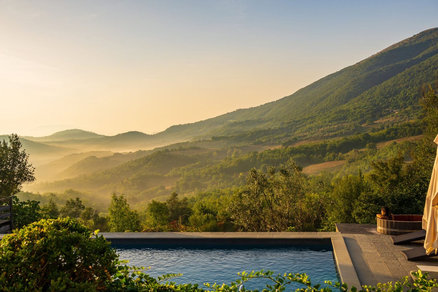 Serene mountain landscape at sunrise featuring lush greenery, rolling hills, and a tranquil swimming pool, perfect for relaxation and outdoor retreats. | Only on SopranoVillas