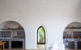 Bright and airy kitchen interior featuring arched alcoves with colorful tile backsplashes, modern appliances, and a large window allowing natural light and garden views. The space combines contemporary design with traditional elements, creating a welcoming atmosphere.