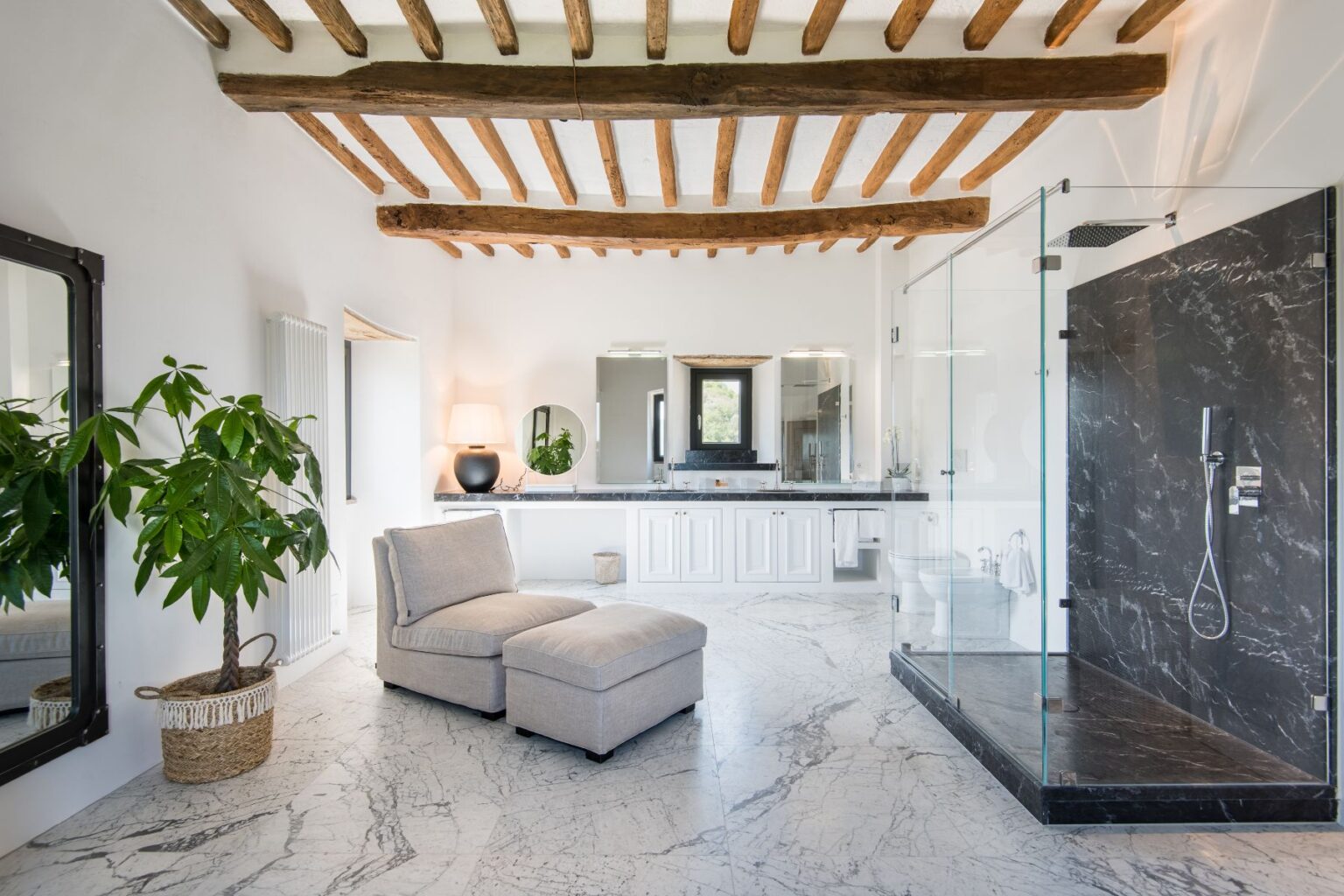 Spacious modern bathroom featuring a glass shower, marble flooring, and wooden beams, with a comfortable chaise lounge and stylish decor elements. | Only on SopranoVillas