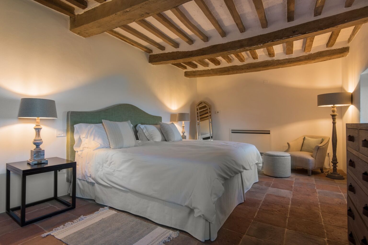 Cozy bedroom featuring a large bed with plush pillows, wooden beams on the ceiling, stylish lamps, and a comfortable seating area, creating a warm and inviting atmosphere. | Only on SopranoVillas