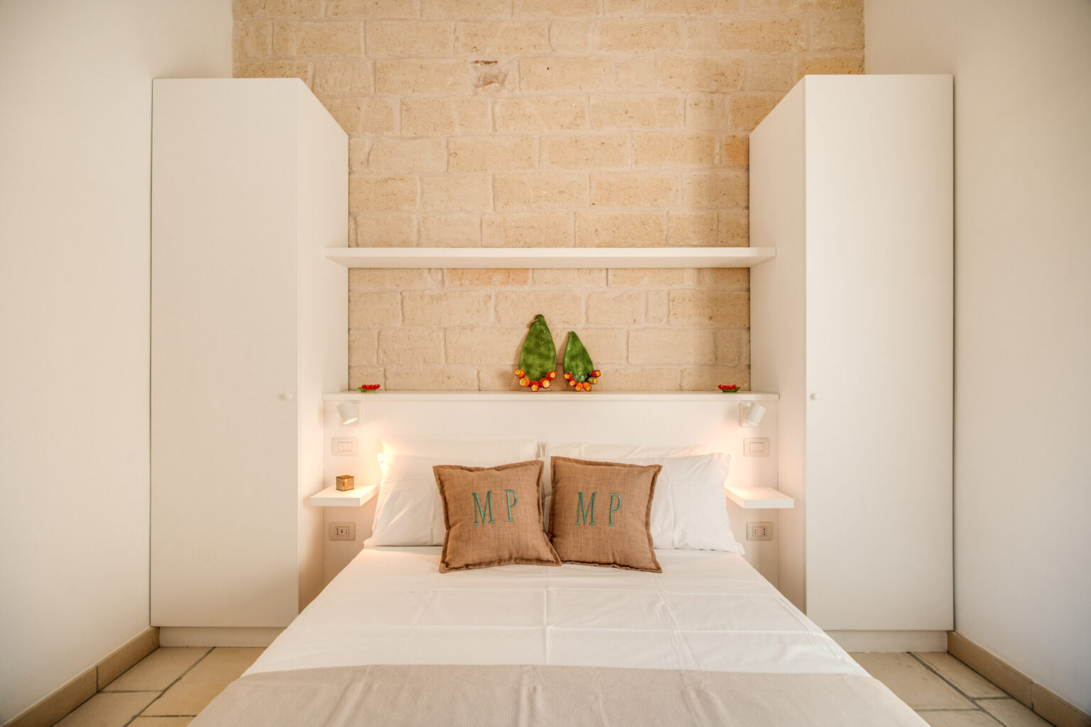 Cozy bedroom with a white bed and decorative pillows, featuring built-in white cabinets and a textured stone wall, creating a modern and inviting atmosphere. | Only on SopranoVillas