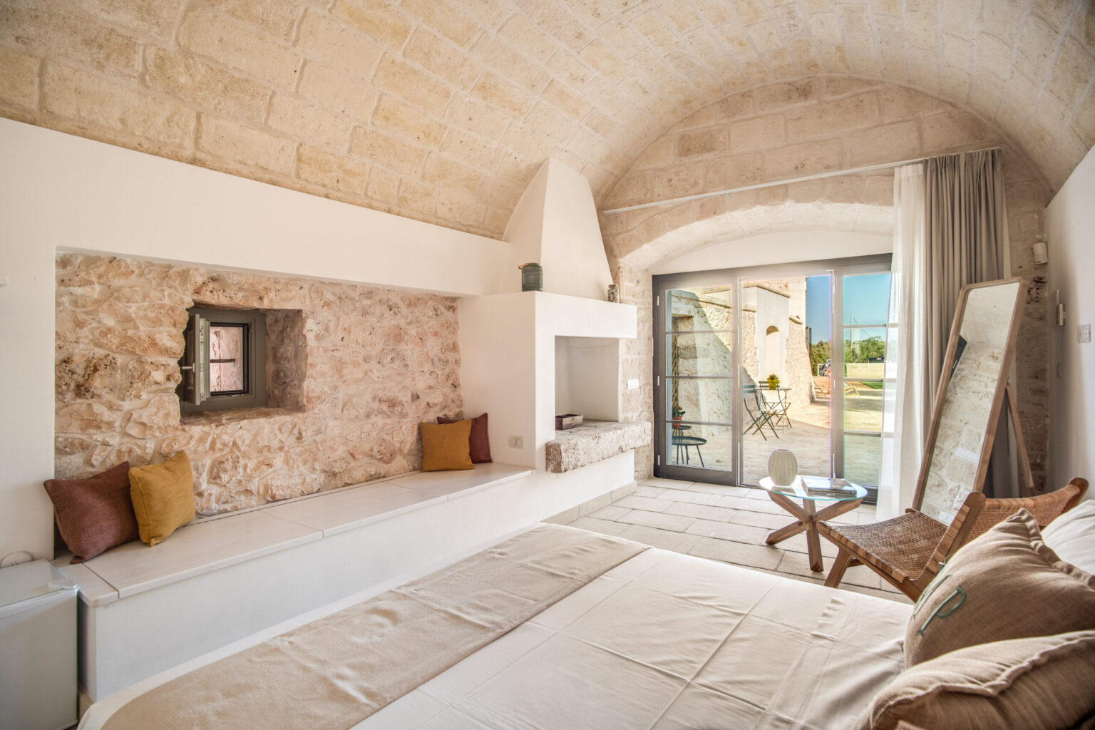 Bright and airy bedroom featuring stone walls, a cozy seating area, and large glass doors leading to an outdoor space. The room is decorated with neutral tones and stylish furnishings, creating a serene and inviting atmosphere. | Only on SopranoVillas