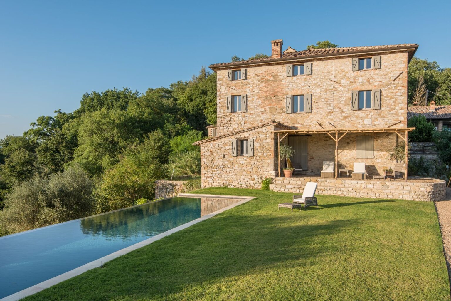 Stone villa with a modern infinity pool set in a lush green landscape, surrounded by trees and a clear blue sky. Ideal for luxury retreats and outdoor relaxation. | Only on SopranoVillas