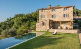 Stone villa with a modern infinity pool set in a lush green landscape, surrounded by trees and a clear blue sky. Ideal for luxury retreats and outdoor relaxation.