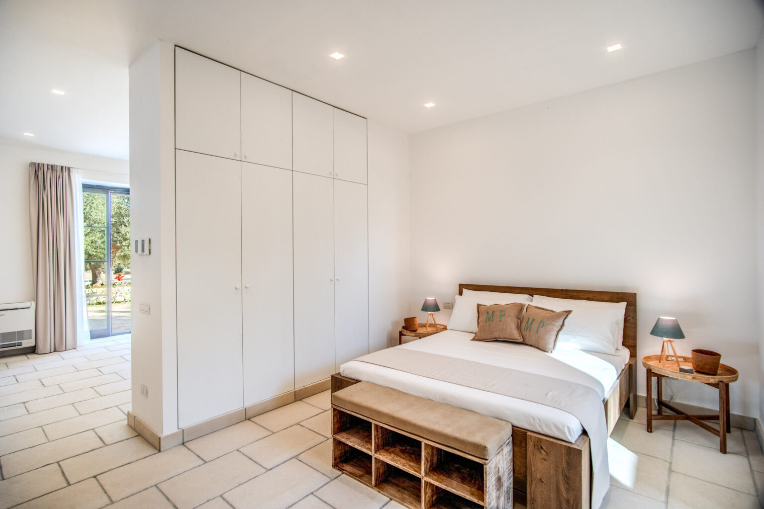 Modern bedroom interior featuring a wooden bed, minimalist decor, built-in wardrobes, and natural light from a nearby window. | Only on SopranoVillas