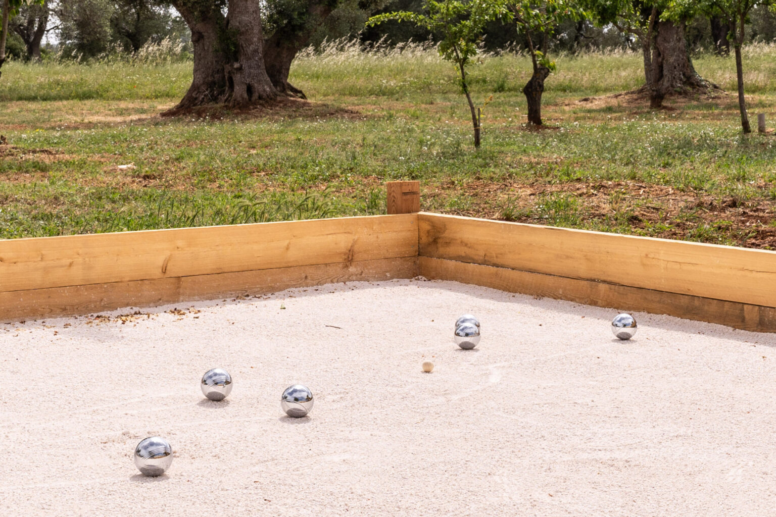 A petanque court featuring metallic balls arranged on sandy ground, surrounded by greenery and trees, ideal for outdoor recreational activities. | Only on SopranoVillas