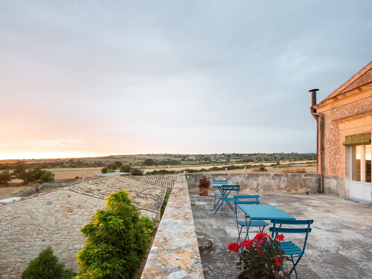 Scenic view from a terrace featuring blue metal chairs and tables, overlooking lush fields and a sunset sky in a rural landscape. | Only on SopranoVillas