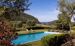 Scenic view of a tranquil swimming pool surrounded by lush greenery and mountains, featuring lounge chairs and a shaded pergola, ideal for relaxation and outdoor leisure.