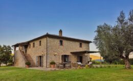 Charming stone farmhouse with a lush green lawn, outdoor seating area, and scenic landscape in the background, ideal for countryside retreats.