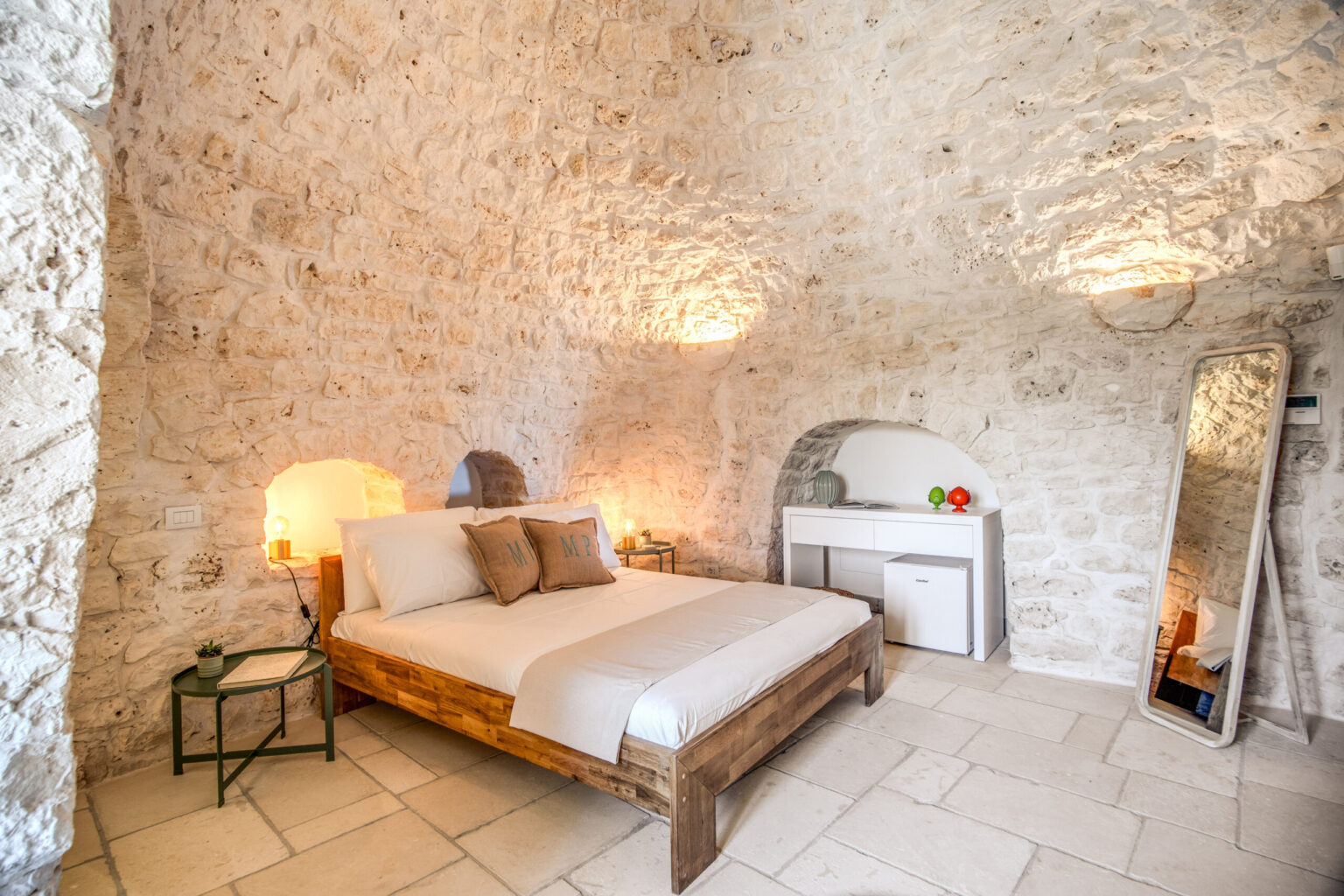 Cozy bedroom with a stone wall design, featuring a wooden bed, decorative pillows, and soft lighting. Includes a mirror and a small table, creating a warm and inviting atmosphere. Ideal for a relaxing getaway. | Only on SopranoVillas