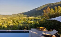 Luxurious outdoor pool area with a stunning mountain view, featuring a wooden hot tub and comfortable lounge chair, surrounded by lush greenery under a clear sky. Perfect for relaxation and enjoying nature.