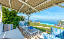 Cozy outdoor seating area with a stunning ocean view, featuring comfortable cushions and a stylish coffee table under a thatched roof. Perfect for relaxation in a luxurious villa setting.