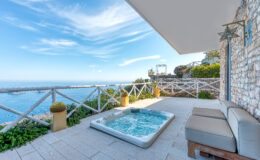 Luxurious outdoor terrace with a hot tub overlooking the ocean, surrounded by greenery and a scenic view of the sky. Perfect for relaxation and enjoying coastal scenery.