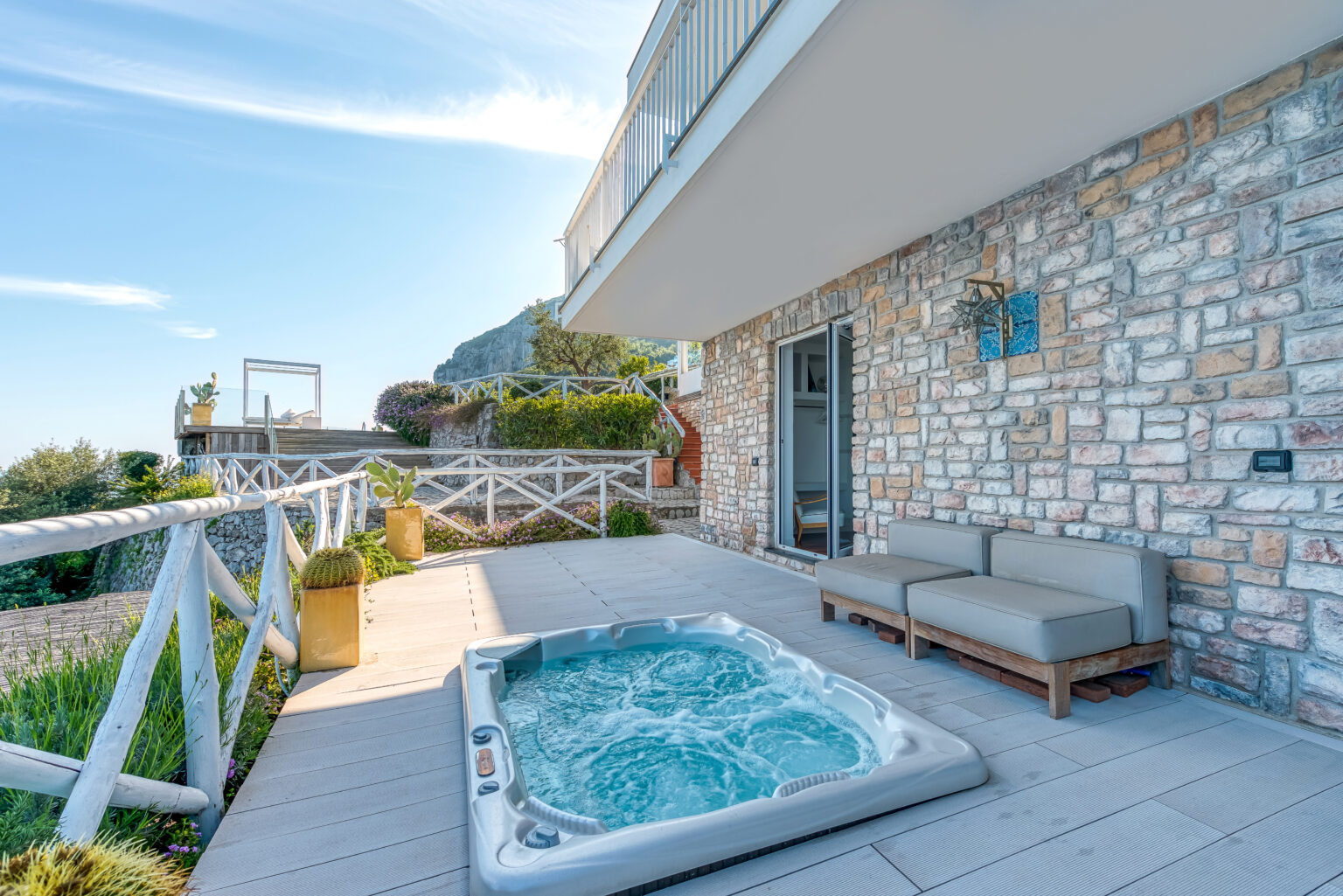 Cozy outdoor patio with a hot tub and comfortable seating, featuring a stunning view of the landscape and clear blue sky. Perfect for relaxation and leisure activities. | Only on SopranoVillas