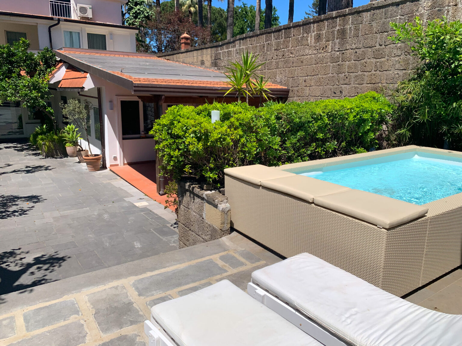 Cozy outdoor space featuring a small pool, lounge chairs, and a charming house surrounded by lush greenery, ideal for relaxation and leisure. | Only on SopranoVillas