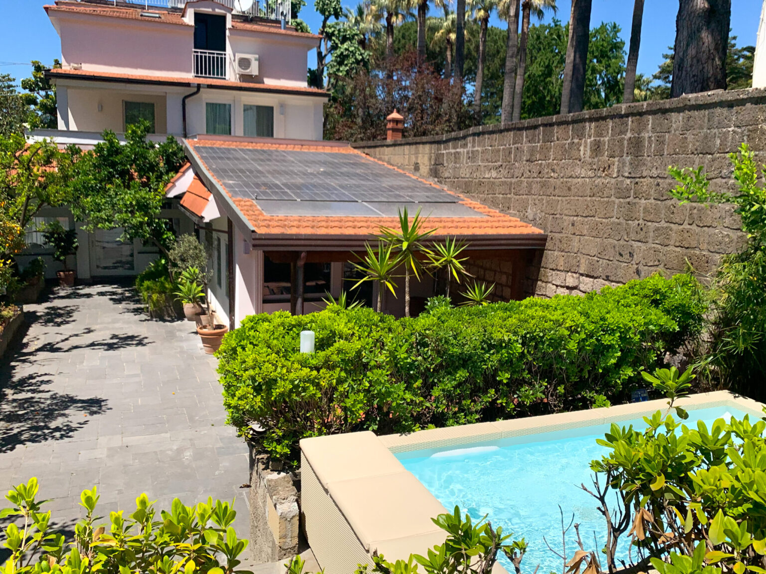 Aerial view of a modern home featuring a solar panel roof, surrounded by lush greenery and a small pool in the foreground, showcasing a tranquil outdoor living space. | Only on SopranoVillas