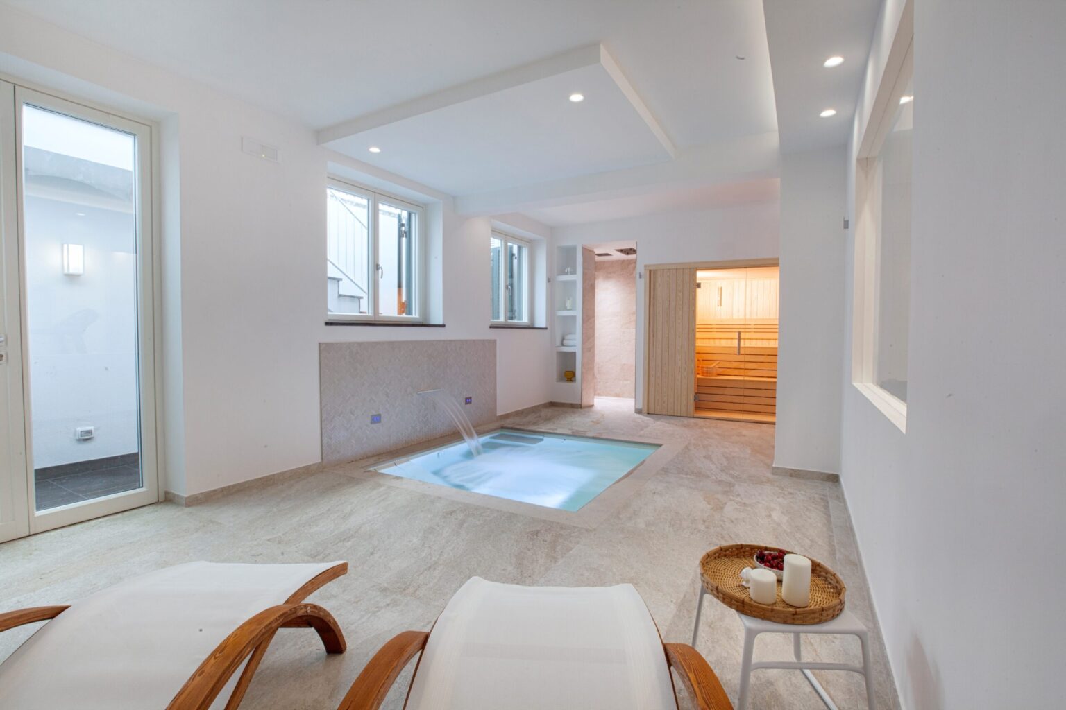 Modern spa interior featuring a private jacuzzi, large windows for natural light, and elegant lounging chairs. The minimalist design emphasizes relaxation and tranquility, ideal for wellness retreats. | Only on SopranoVillas