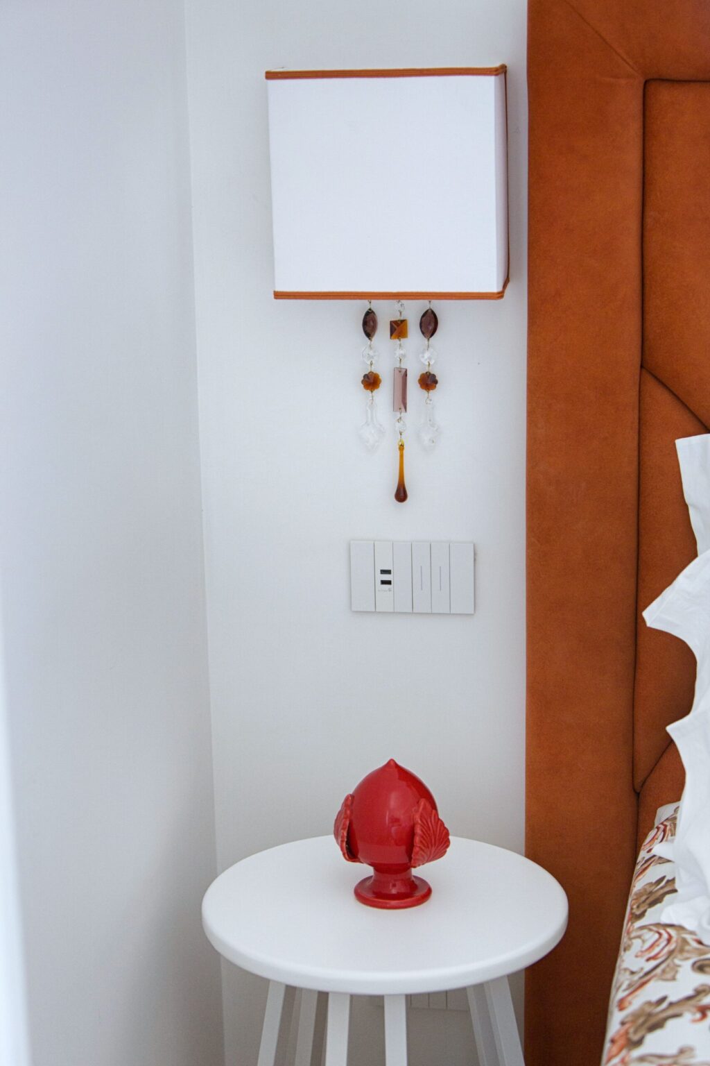 Interior view of a modern room featuring a decorative wall hanging, a light switch panel, and a textured orange accent wall, showcasing contemporary design elements. | Only on SopranoVillas