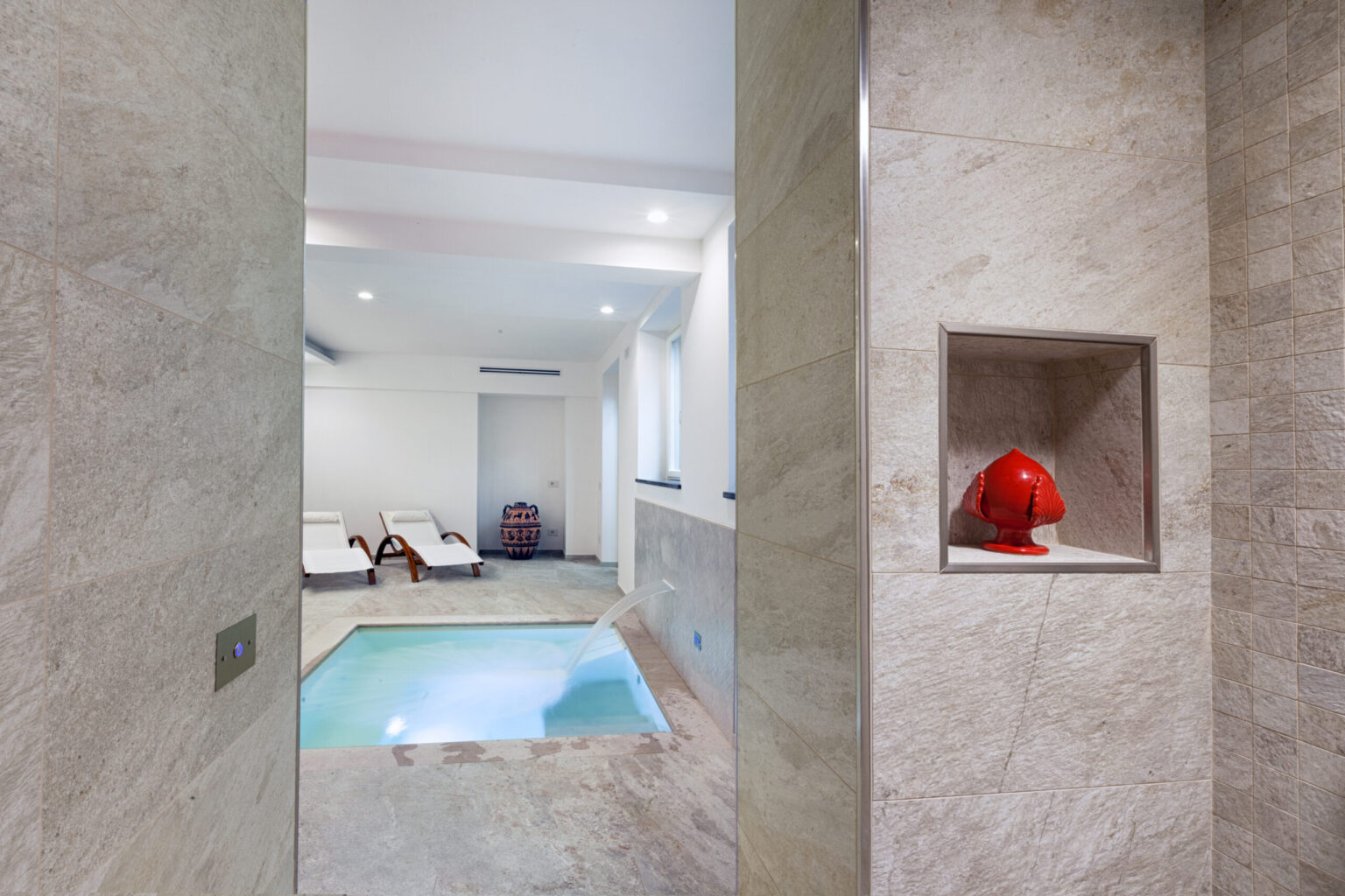 Luxurious indoor spa area featuring a small private pool, elegant marble walls, and a vibrant red decorative figure on a shelf, creating a serene and stylish ambiance. | Only on SopranoVillas