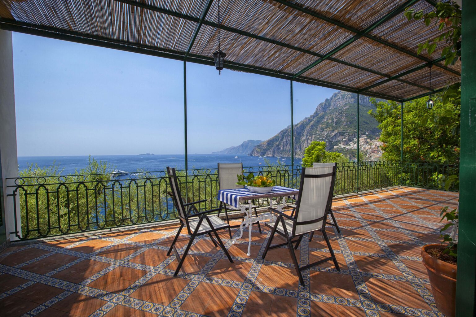 Scenic terrace with two chairs and a table overlooking the ocean and mountains, featuring a shaded area with bamboo roofing. Ideal for relaxation and enjoying coastal views. | Only on SopranoVillas