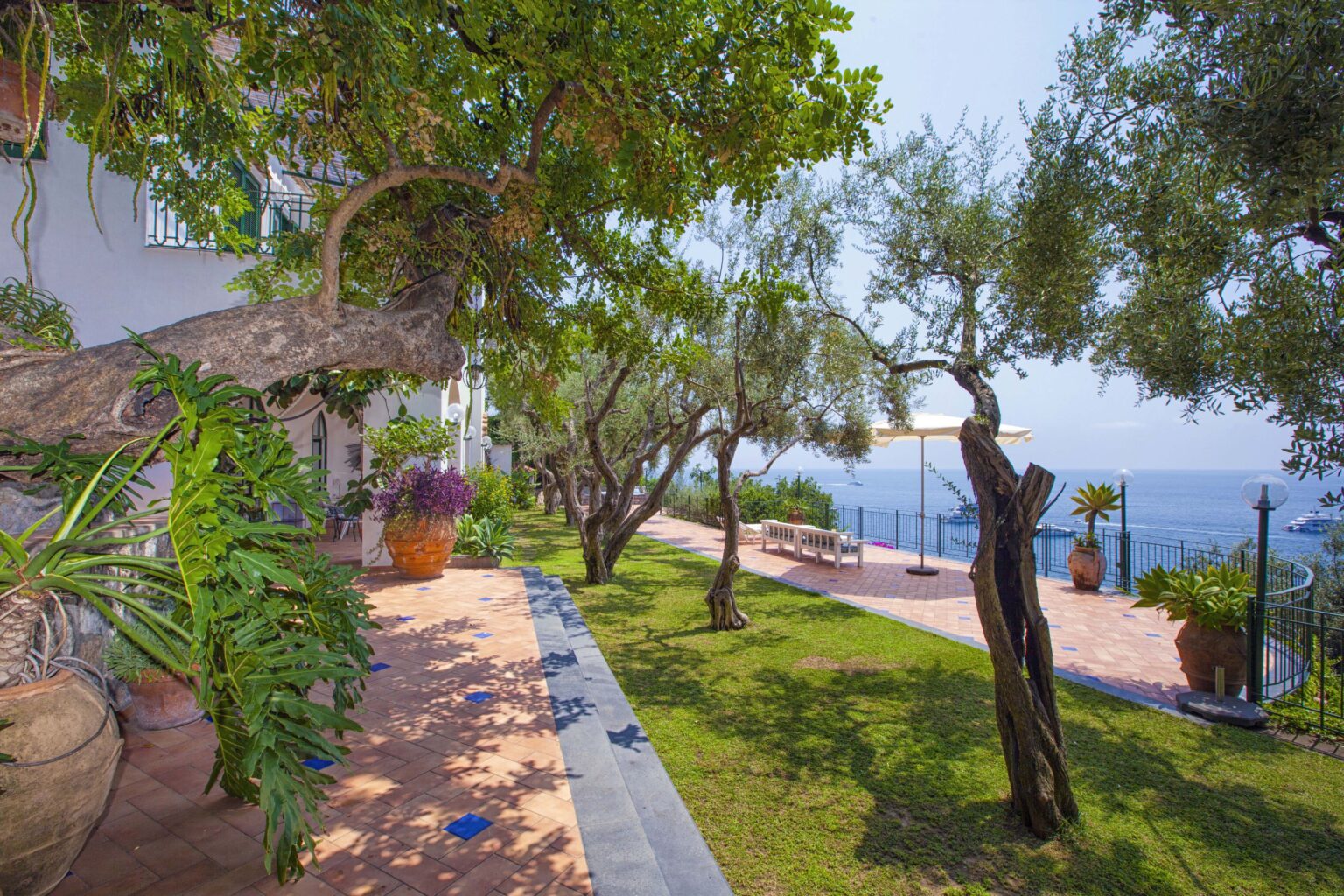 Luxury villa garden in Italy featuring lush greenery, olive trees, and stunning sea views, perfect for a relaxing getaway. Ideal for vacation rentals. | Only on SopranoVillas