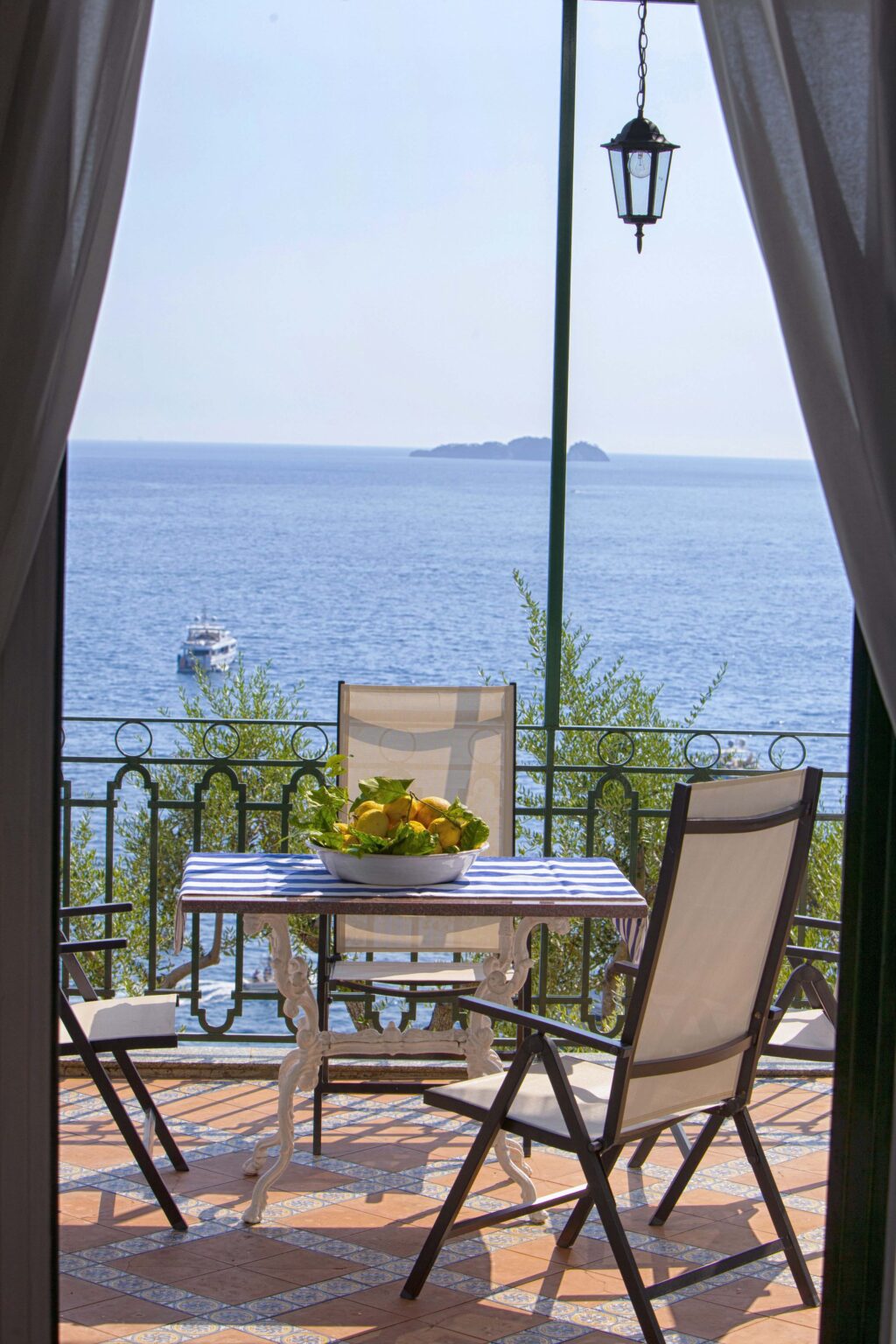 Luxury villa rental in Italy featuring a scenic balcony view of the serene sea, with a table set for dining and lush greenery in the background. Ideal for relaxing getaways. | Only on SopranoVillas