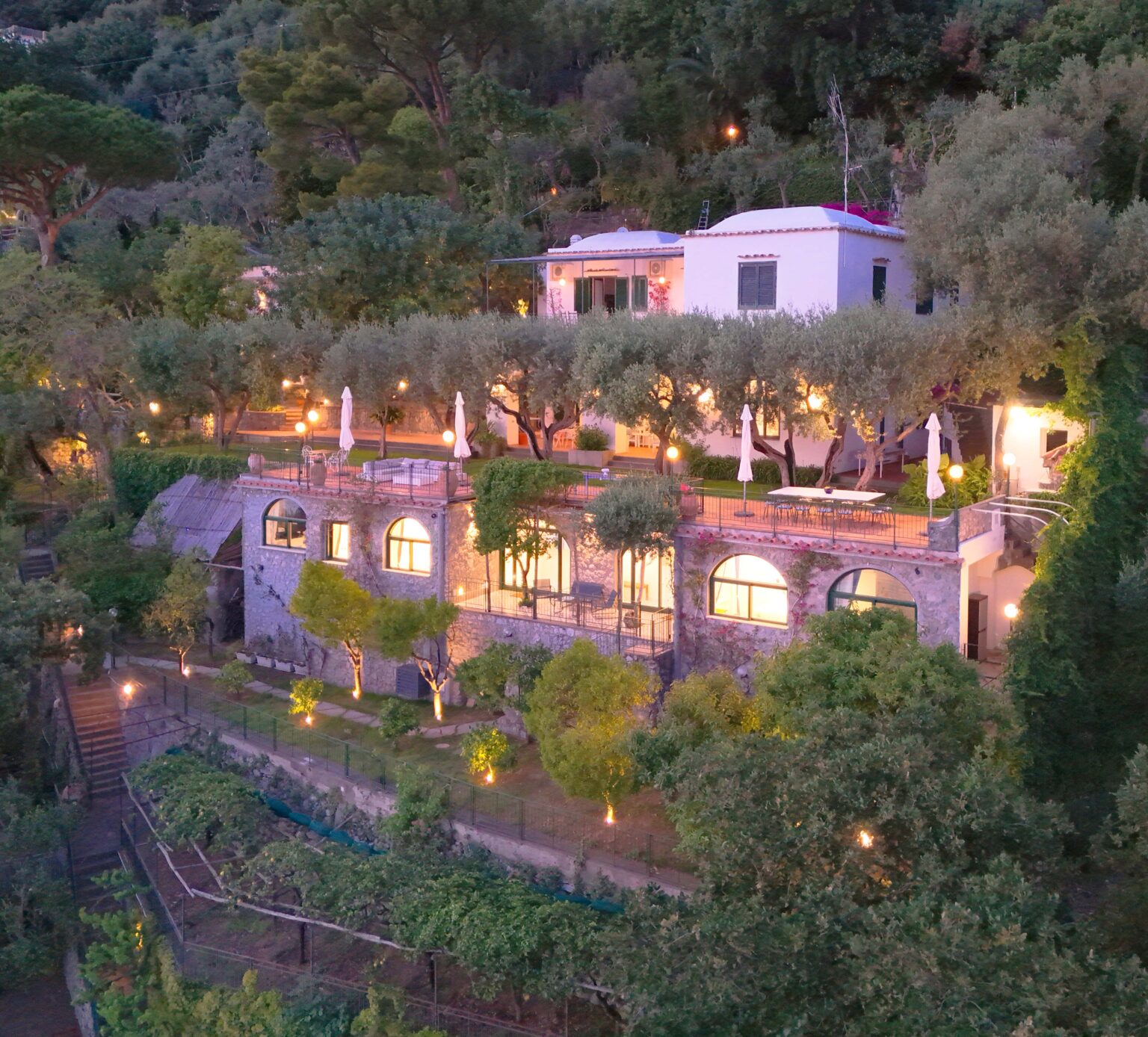 Luxury villa for rent in Italy, featuring elegant architecture, lush gardens, and ambient lighting, set against a serene hillside backdrop. Ideal for a relaxing getaway, offering stunning views and premium amenities. | Only on SopranoVillas