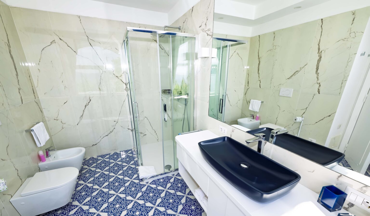 Luxurious bathroom in an Italian villa for rent, featuring modern fixtures, elegant marble walls, a spacious shower, and stylish blue patterned tiles. | Only on SopranoVillas
